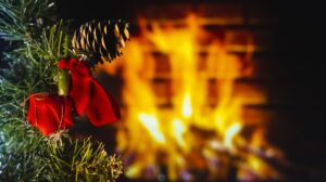 A closeup image of a Christmas tree with a pine cone and a blazing fire in the background.